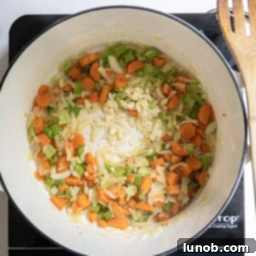 Rustic Italian Minestrone 4 Chopped carrots, celery, and onion, known as mirepoix, are shown sautéing in a large Dutch oven with minced garlic, releasing their aromatic flavors.