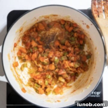 Rustic Italian Minestrone 5 Tomato paste is being stirred into the softened mirepoix vegetables in a pot, creating a rich caramelized base for the minestrone soup.