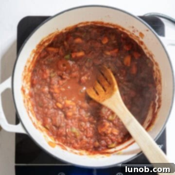 Rustic Italian Minestrone 6 Crushed tomatoes are added to the pot with the caramelized vegetables and tomato paste, simmering gently to develop the soup's base.