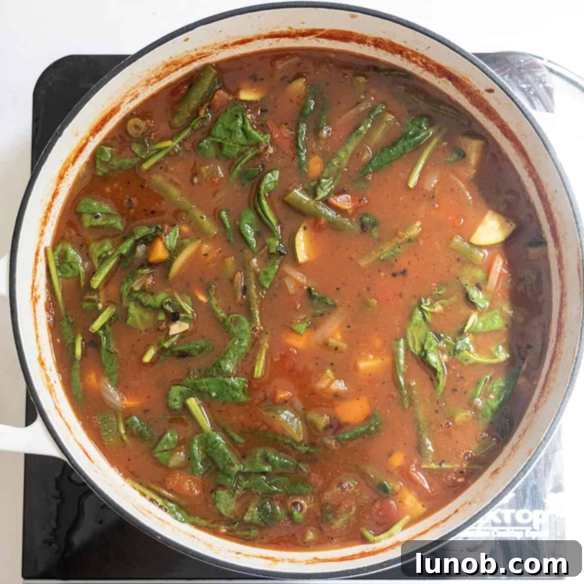 Rustic Italian Minestrone 8 Fresh spinach is stirred into the hot minestrone soup, beginning to wilt into the vibrant vegetable broth.