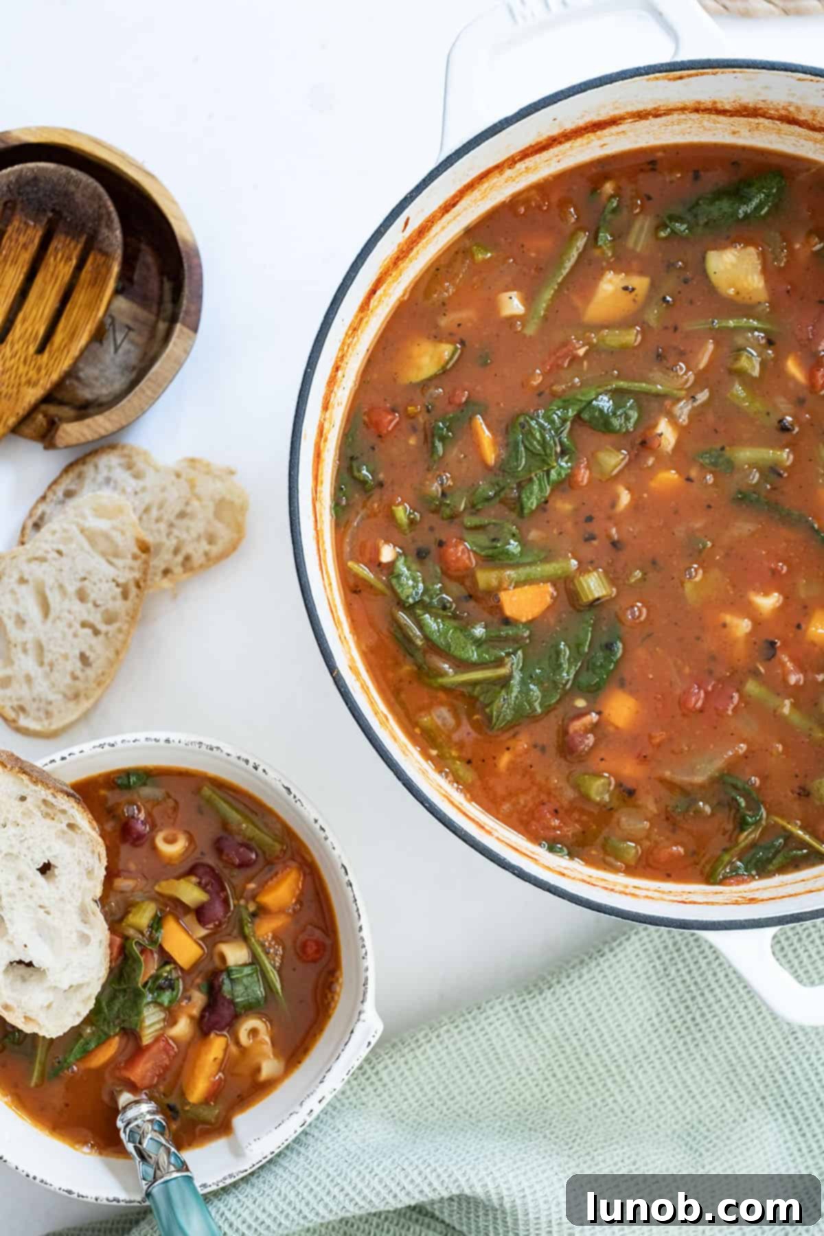 Rustic Italian Minestrone 9 A generous serving of classic Italian minestrone soup in a rustic bowl, alongside the large Dutch oven it was cooked in, brimming with more soup, and a side of Italian bread.