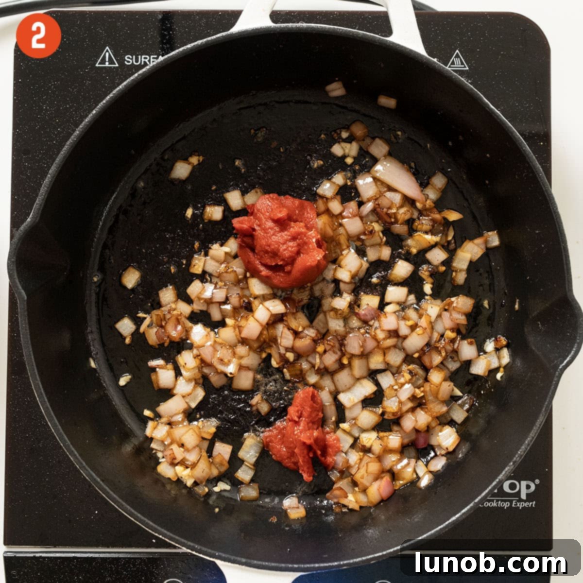 Tomato paste caramelizing with sautéed shallots and garlic in the saucepan, deepening in color and flavor.