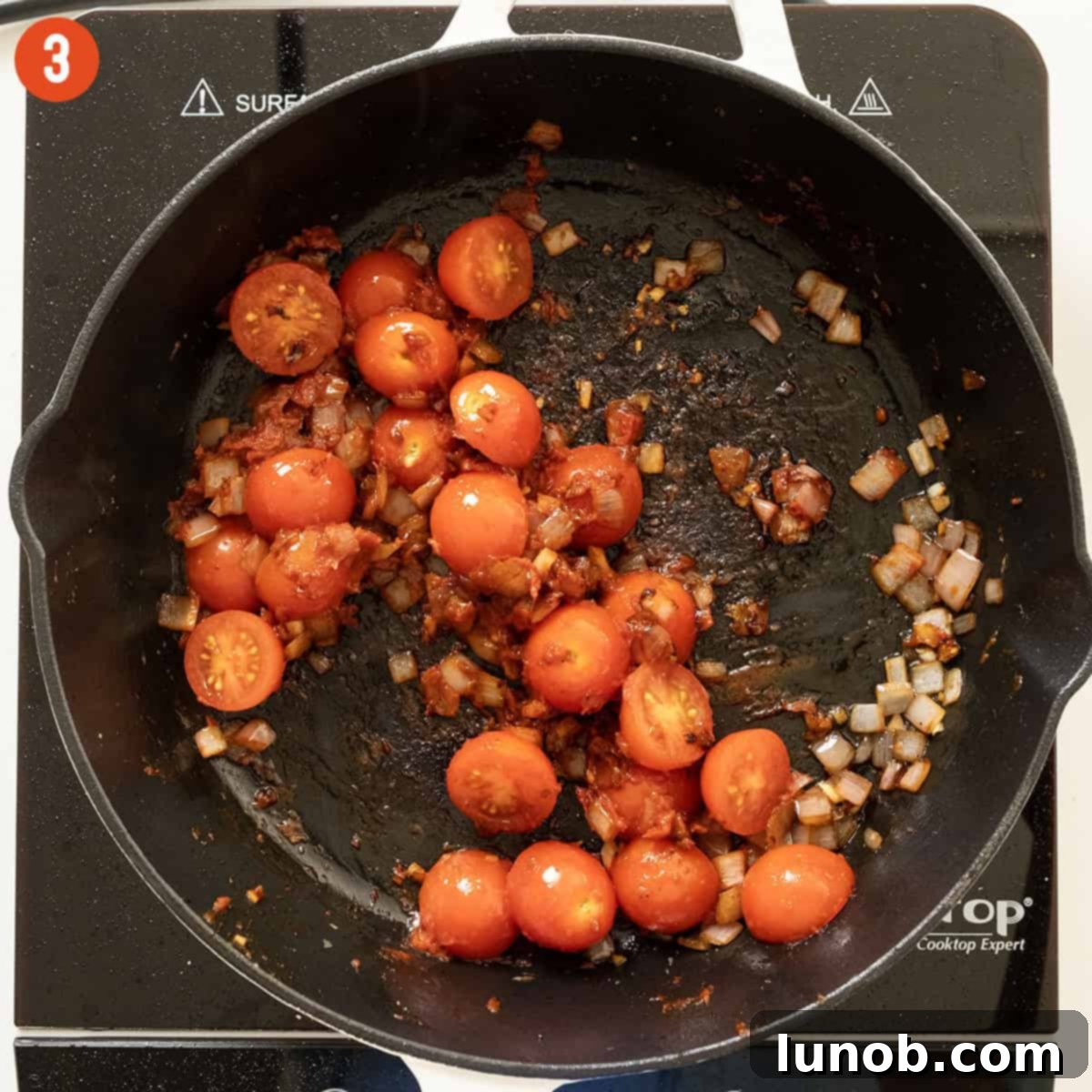 Halved cherry tomatoes sautéing in the saucepan with the aromatic base, their skins beginning to wrinkle and burst.