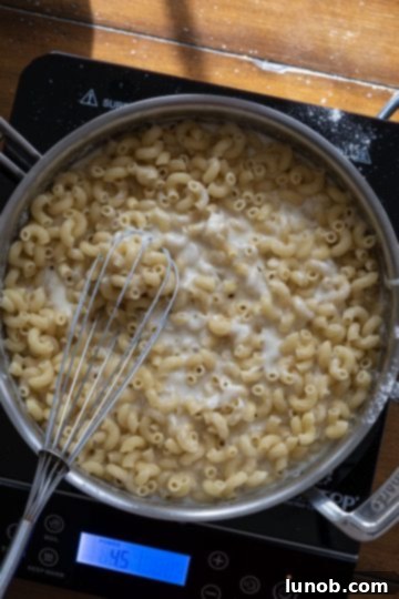 Italian Comfort Mac and Cheese 7 Cooked macaroni being added to the creamy cheese sauce in a saucepan