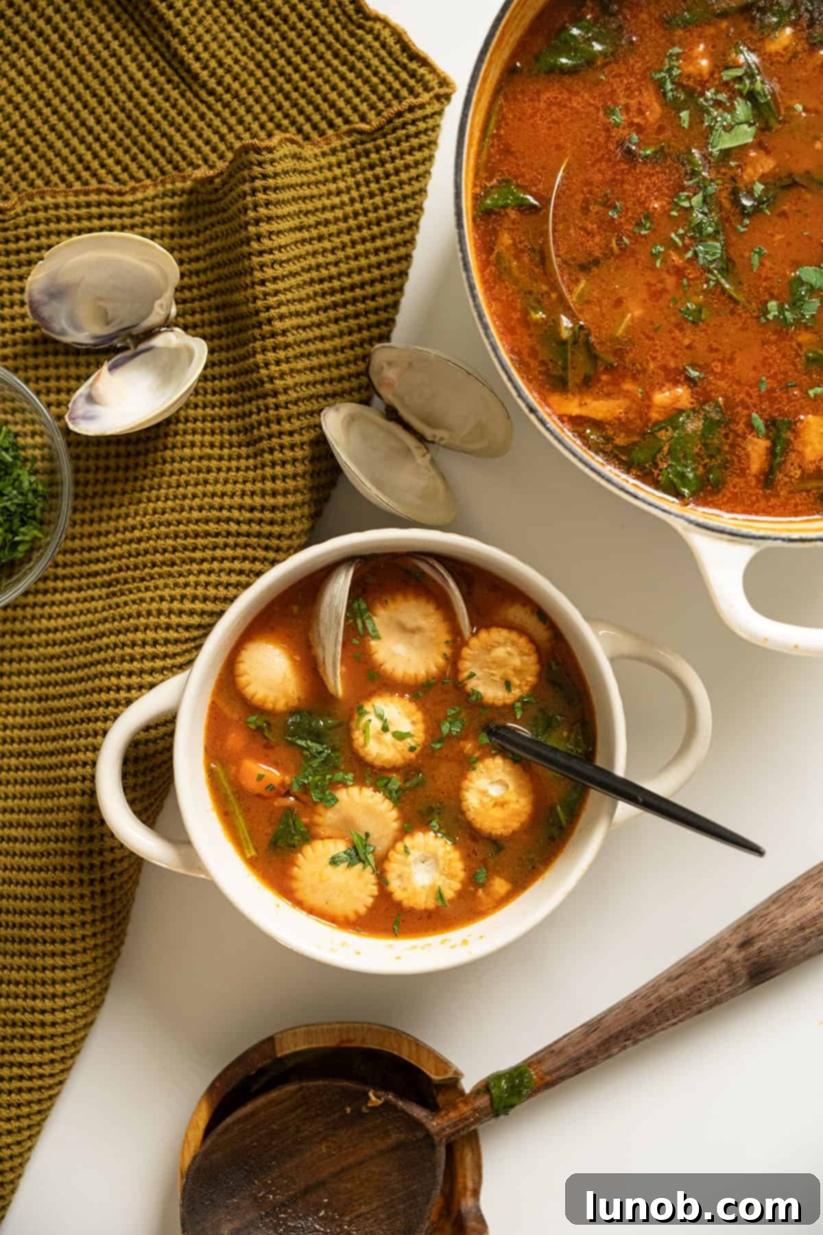 Manhattan clam chowder topped with oyster crackers, next to the pot of soup.