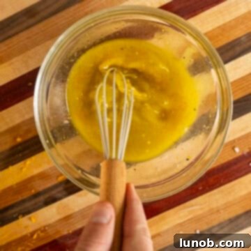 Whisking orange vinaigrette dressing in a bowl, showing the emulsification process.