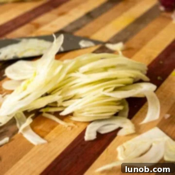 Thinly shaved fennel on a wooden cutting board, ready for the salad.