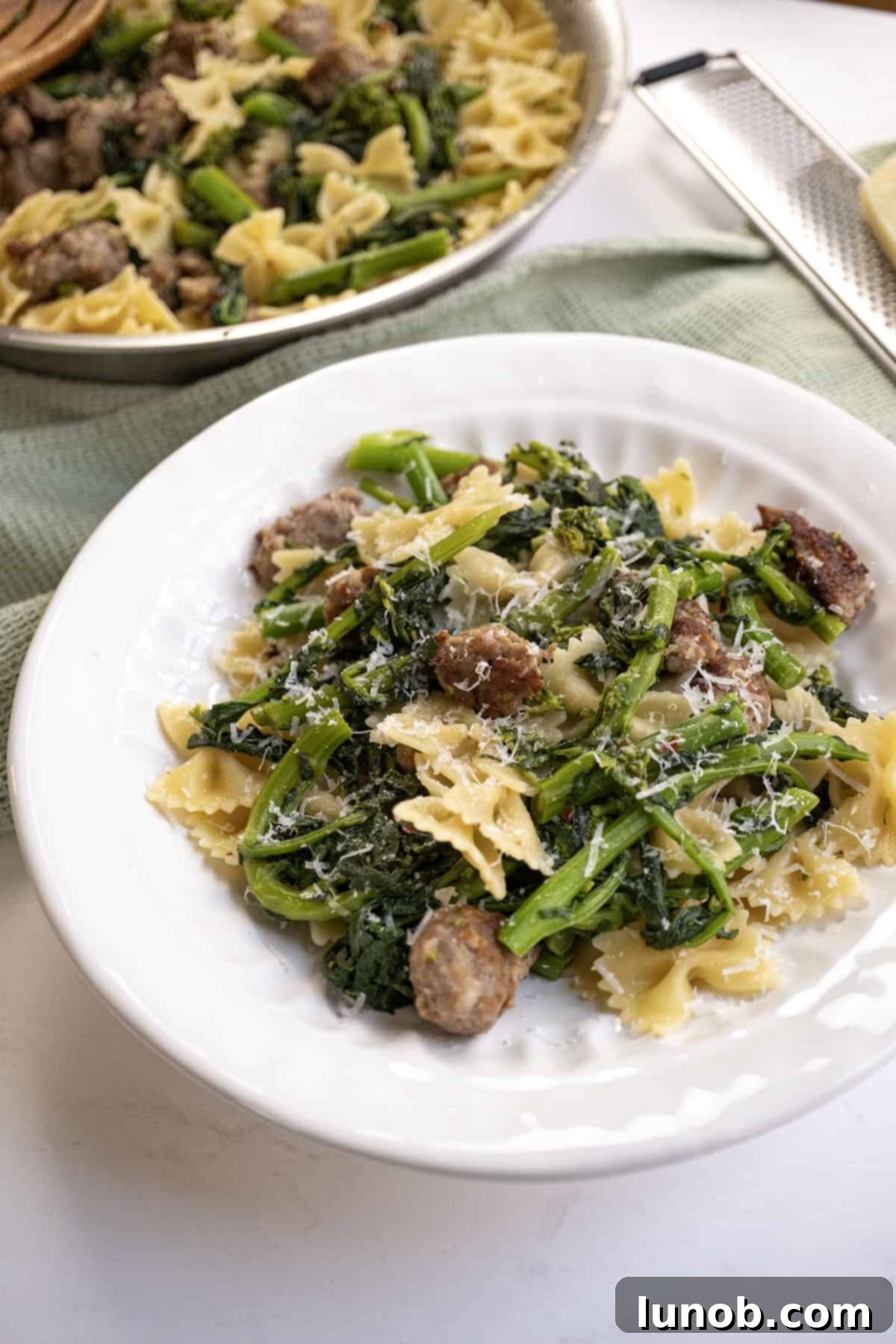 Farfalle with savory Italian sausage and vibrant broccoli rabe, elegantly topped with grated parmesan cheese on a white plate, ready to be enjoyed.