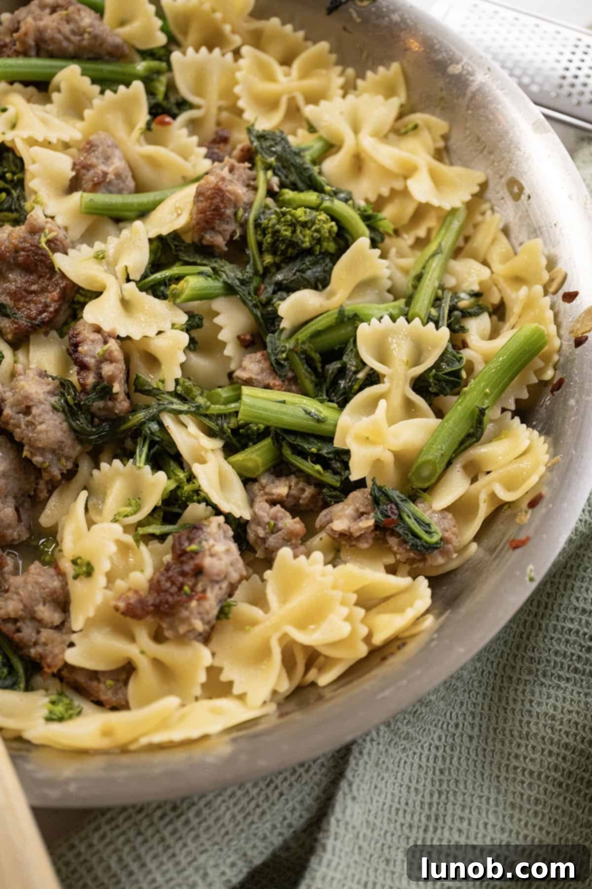 A generous serving of farfalle pasta with sausage and broccoli rabe, piled high on a plate and topped with an abundance of freshly grated parmesan cheese, ready to be enjoyed.