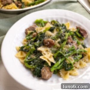 Farfalle with sausage and broccoli rabe, topped with parmesan on a plate.