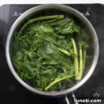 Fresh broccoli rabe being blanched in a pot of boiling water to remove bitterness and prepare for the pasta dish.