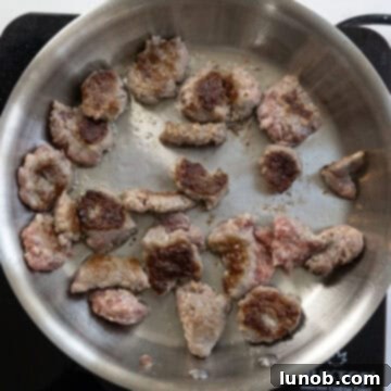 Seared ground sausage pieces in a pan, flipped to achieve browning on all sides, ready for further breakdown.