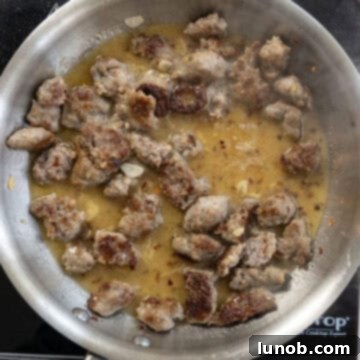 White wine being poured into the pan with seared sausage, garlic, and red pepper, deglazing the pan and forming the sauce base.