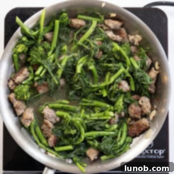 Chopped broccoli rabe added to the simmering sausage and white wine sauce, ready to absorb the rich flavors.