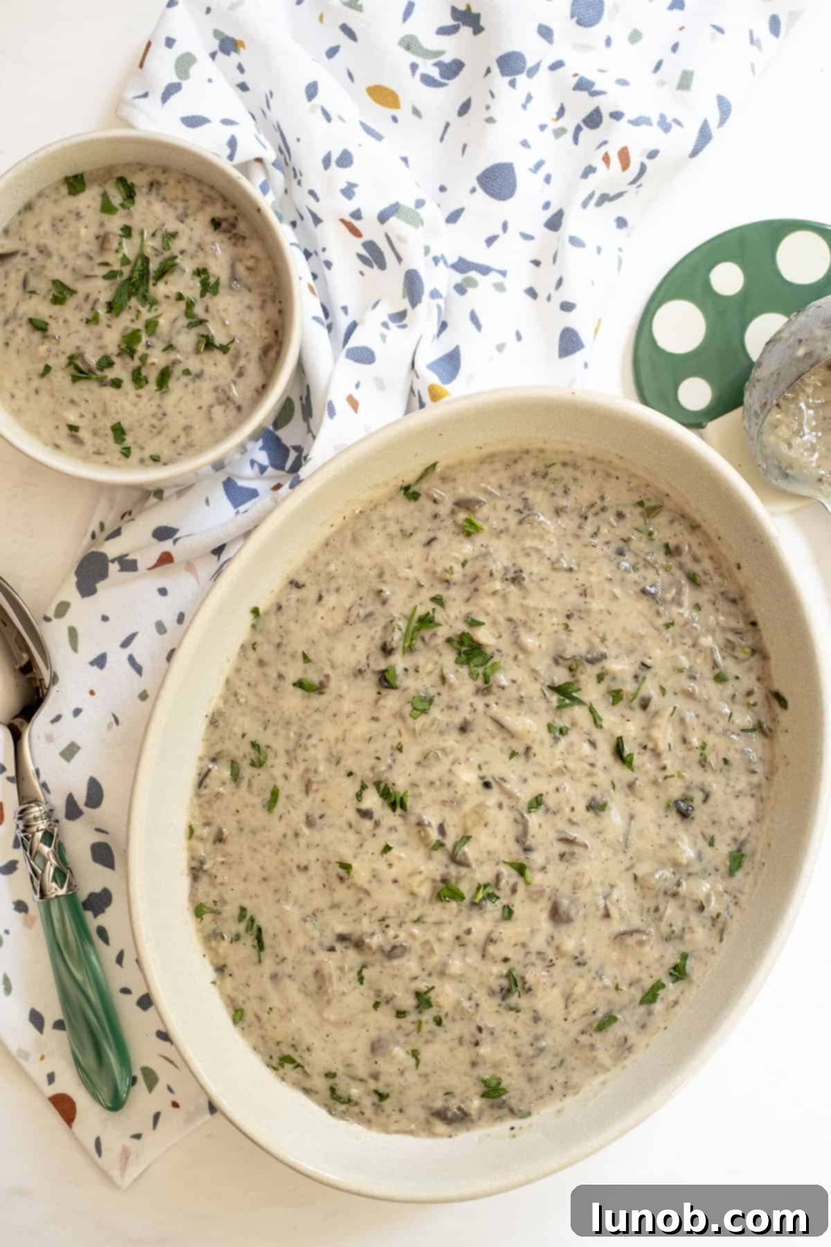 Mushroom soup in a large serving bowl and a small cup on the side, garnished. 