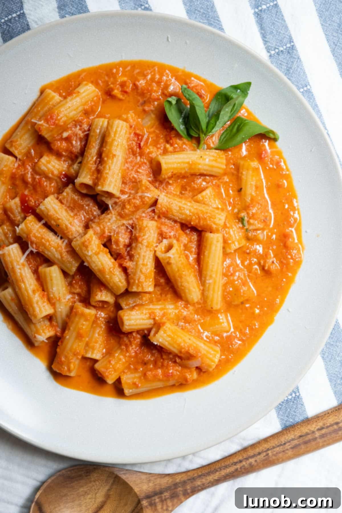 Rigatoni pasta generously coated with vibrant creamy red pepper sauce, garnished with fresh basil.