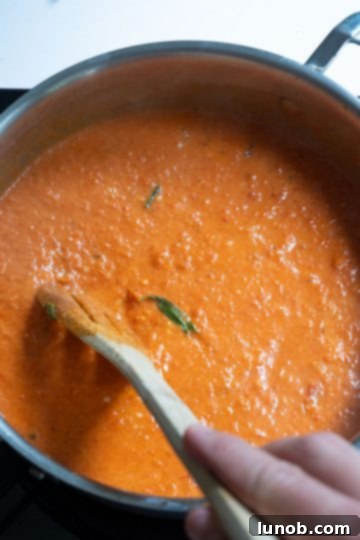 Creamy red pepper sauce, now orange-pink, in a saucepan after heavy cream has been stirred in.