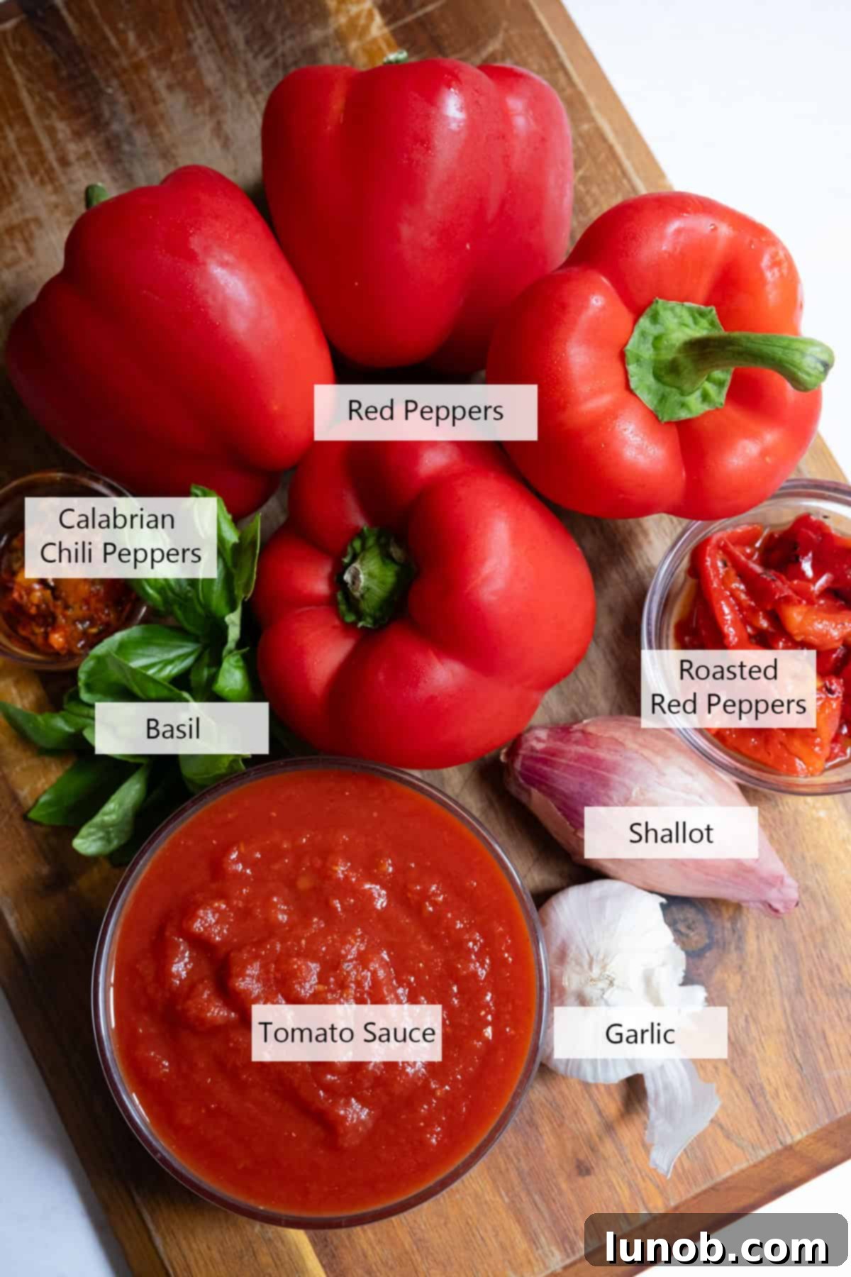 Fresh red peppers, jarred roasted red peppers, garlic, shallots, basil, and a can of tomatoes on a cutting board, ready for the creamy red pepper sauce recipe.