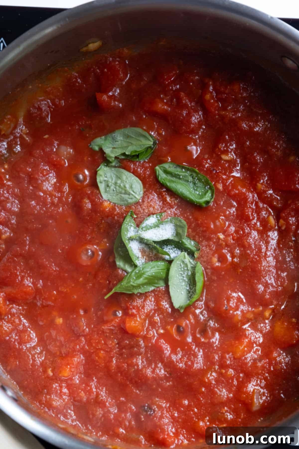Tomato base with basil simmering gently in a large pan on the stovetop.