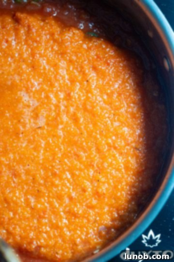 Blended red pepper and tomato sauce combined and simmering in a pan.