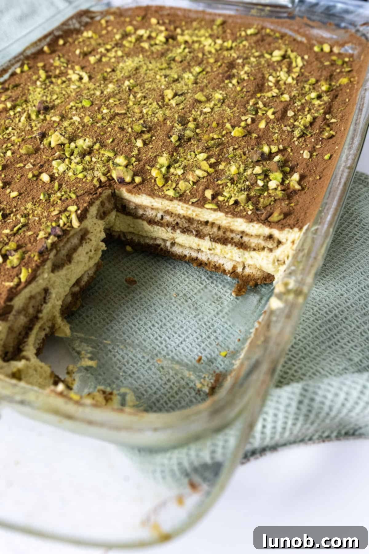 The tray of tiramisu with a square cut out, showcasing its layers of cream and ladyfingers.
