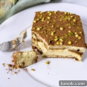 A beautiful slice of Pistachio Cream Tiramisu on a plate, with a spoonful scooped out.