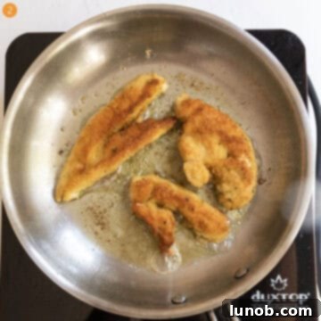 Golden brown breaded chicken tenderloins frying in olive oil in a saucepan.
