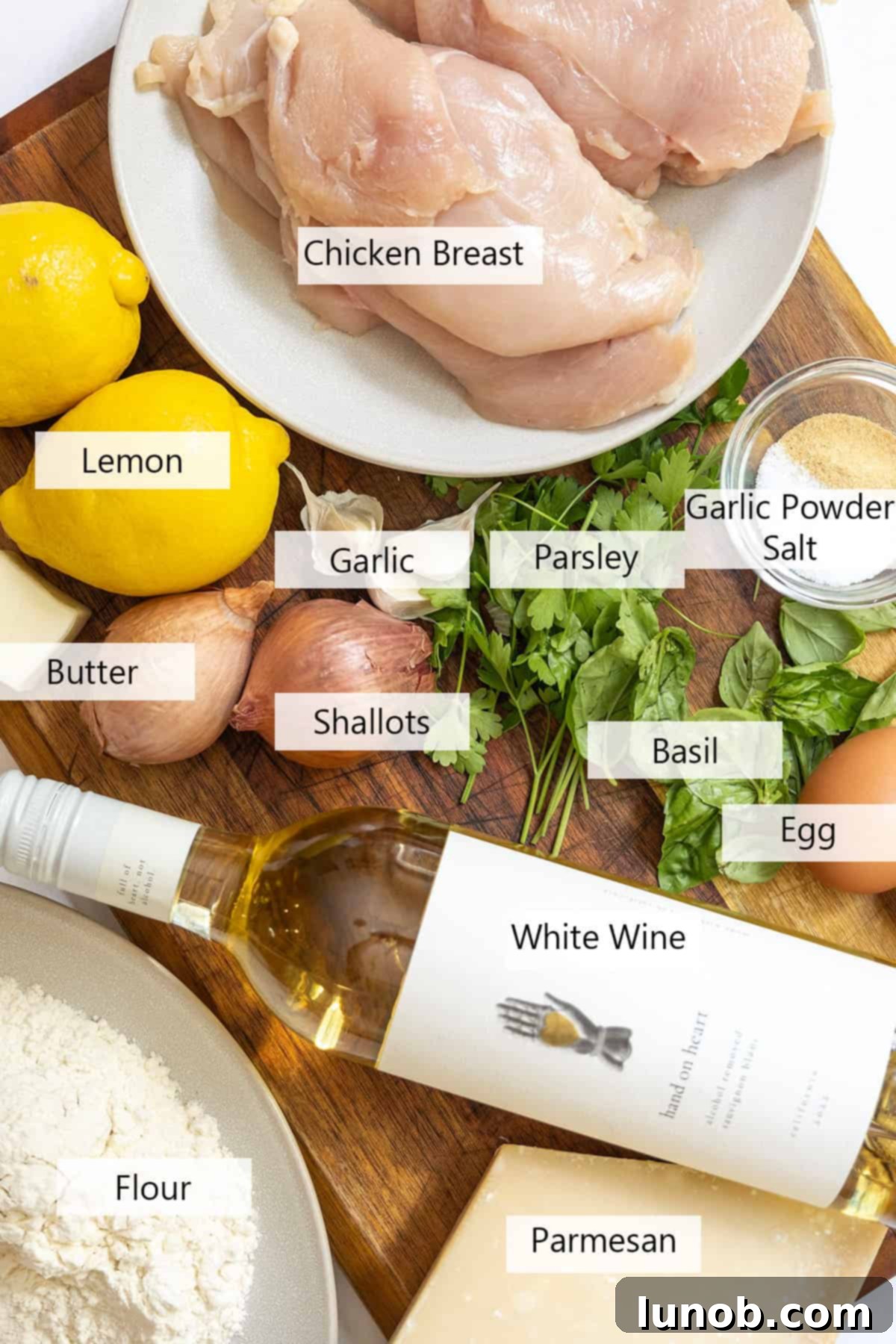Gourmet Chicken Francese 3 Fresh ingredients laid out for making Chicken Francese: chicken breasts, lemons, garlic, shallot, parsley, white wine, chicken broth, olive oil, flour, garlic powder, eggs, parmesan, salt, and basil.