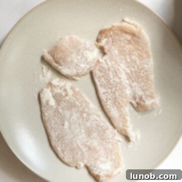 Gourmet Chicken Francese 4 Chicken cutlets being dredged in a plate of flour and garlic powder mixture.