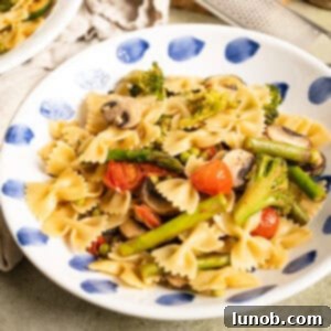 Pasta primavera with broccoli, asparagus, and cherry tomatoes in a bowl, garnished with parmesan.