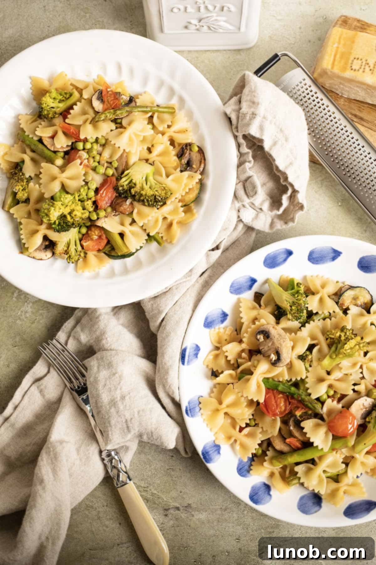 Two bowls filled with pasta primavera, served with a side of grated parmesan cheese.
