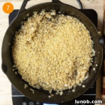 One-Pan Lemon Chicken Orzo Skillet 7 Orzo pasta added to the pan and combined with sautéed onions, garlic, and reduced white wine, turning golden.