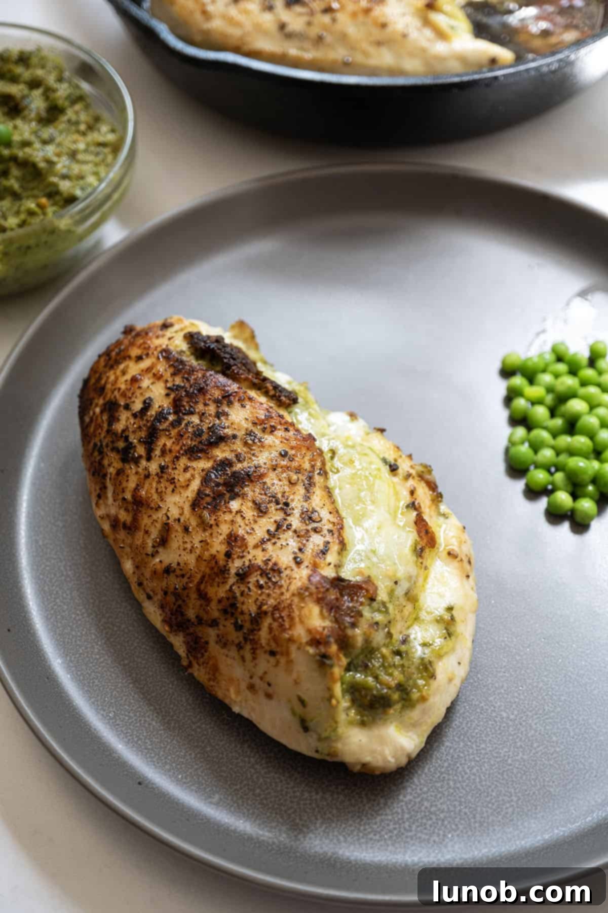 Irresistible Pesto Stuffed Chicken 2 Pesto stuffed chicken on a plate with peas, showcasing a perfectly seared crust and melty cheese.