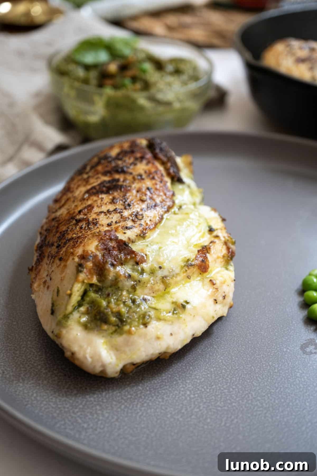 Irresistible Pesto Stuffed Chicken 10 Close-up of pesto stuffed chicken on a plate, garnished with fresh peas and basil, ready to be enjoyed.