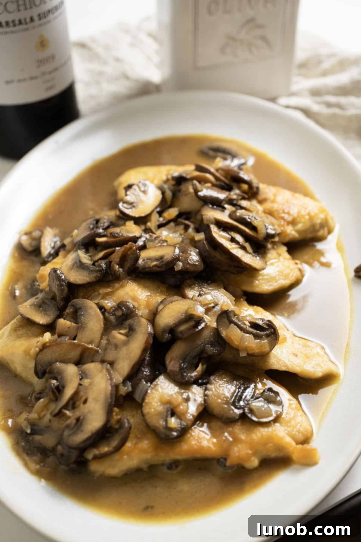 Gourmet Chicken Marsala 12 Chicken marsala with mushroom sauce served over the top of the chicken on a plate.