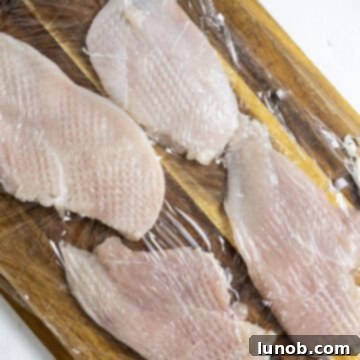 Gourmet Chicken Marsala 4 Sliced chicken breast with saran wrap over it being tenderized.