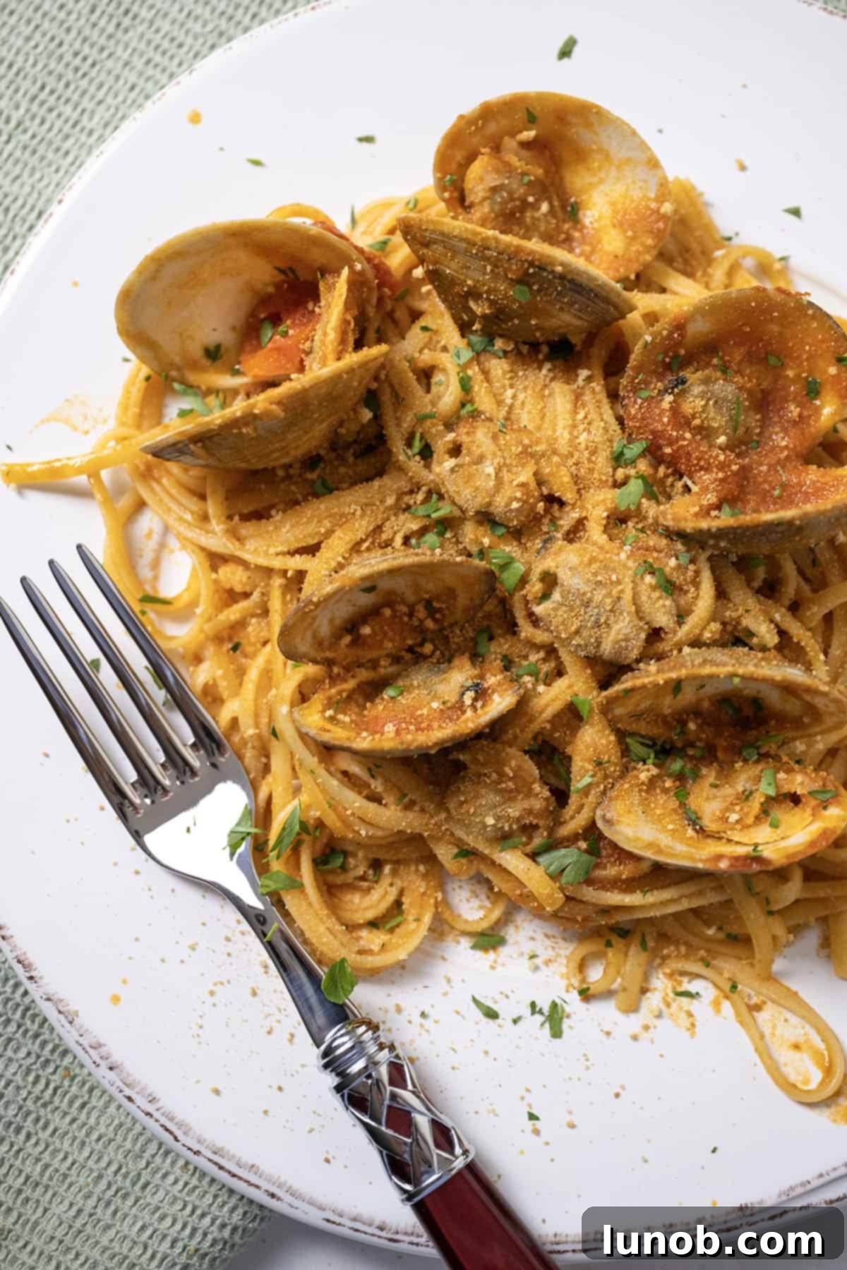 A plate of linguine with clams in a vibrant red sauce, garnished with fresh herbs and toasted breadcrumbs, ready to be served.