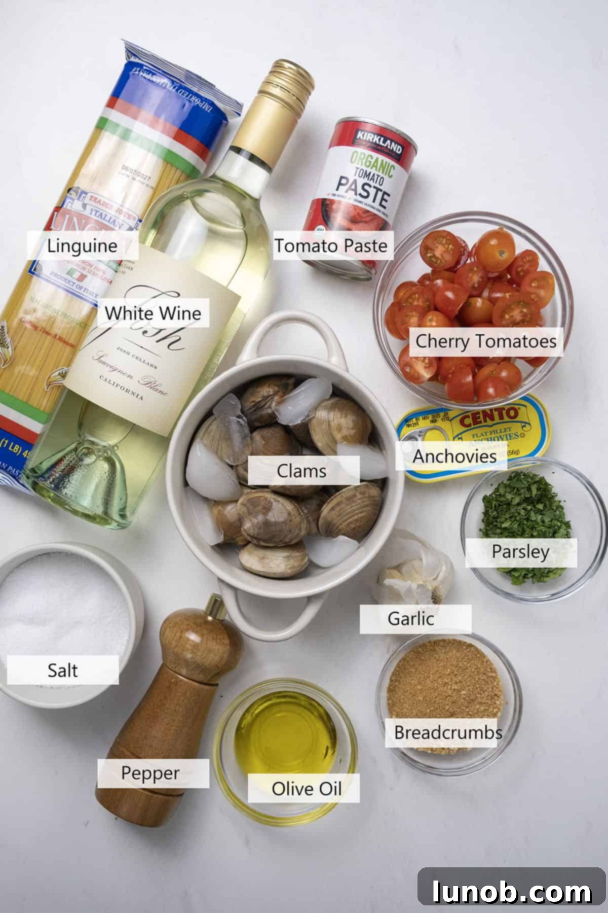 Various fresh ingredients for linguine with red clam sauce laid out on a wooden surface, including cherry tomatoes, garlic, clams, and herbs.