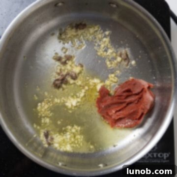 Tomato paste caramelizing in a saucepan with garlic and anchovy oil.