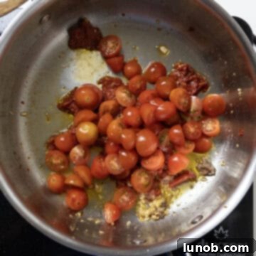 Halved cherry tomatoes added to the rich tomato paste base in the saucepan.