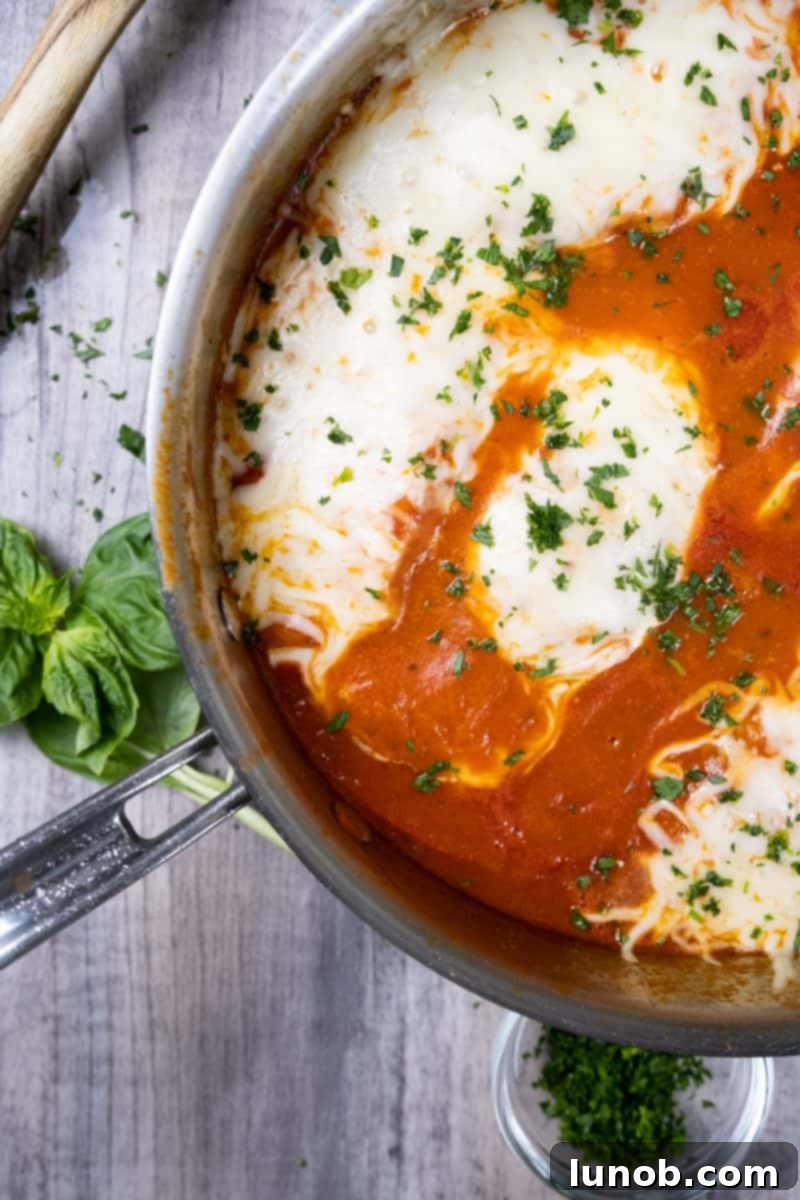 Ultimate Chicken Pizzaiola 2 Delectable Chicken Pizzaiola garnished with fresh parsley and basil, showcasing melted mozzarella and a rich tomato sauce with peppers.