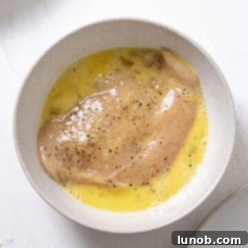 Ultimate Chicken Pizzaiola 4 Thinly sliced chicken breast being dipped in a rich egg wash, ready for coating.