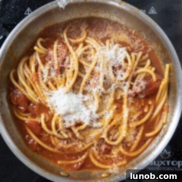 Bucatini combined with sauce and topped with grated pecorino romano in a saucepan, off the heat.