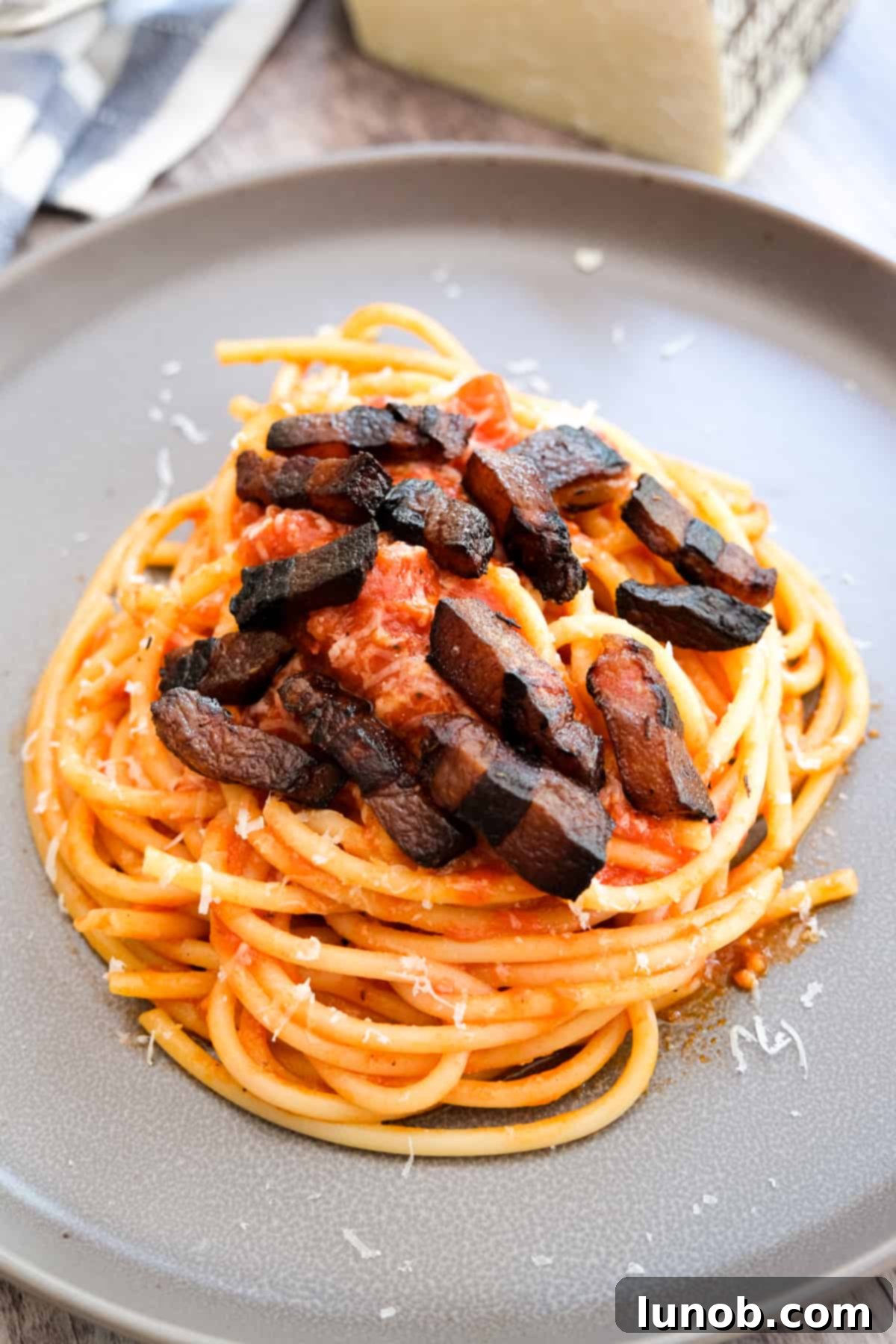 A generously plated serving of Bucatini Amatriciana, garnished with crispy guanciale and fresh Pecorino Romano.