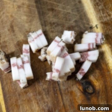 Guanciale cut into strips and laid out on a cutting board, ready for frying.