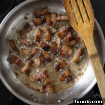 Crispy golden brown guanciale frying in its rendered fat in a saucepan.