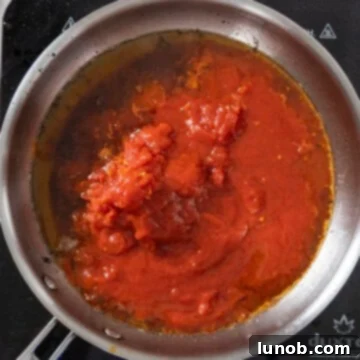 Whole peeled plum tomatoes being hand-squeezed into the guanciale oil in a saucepan.