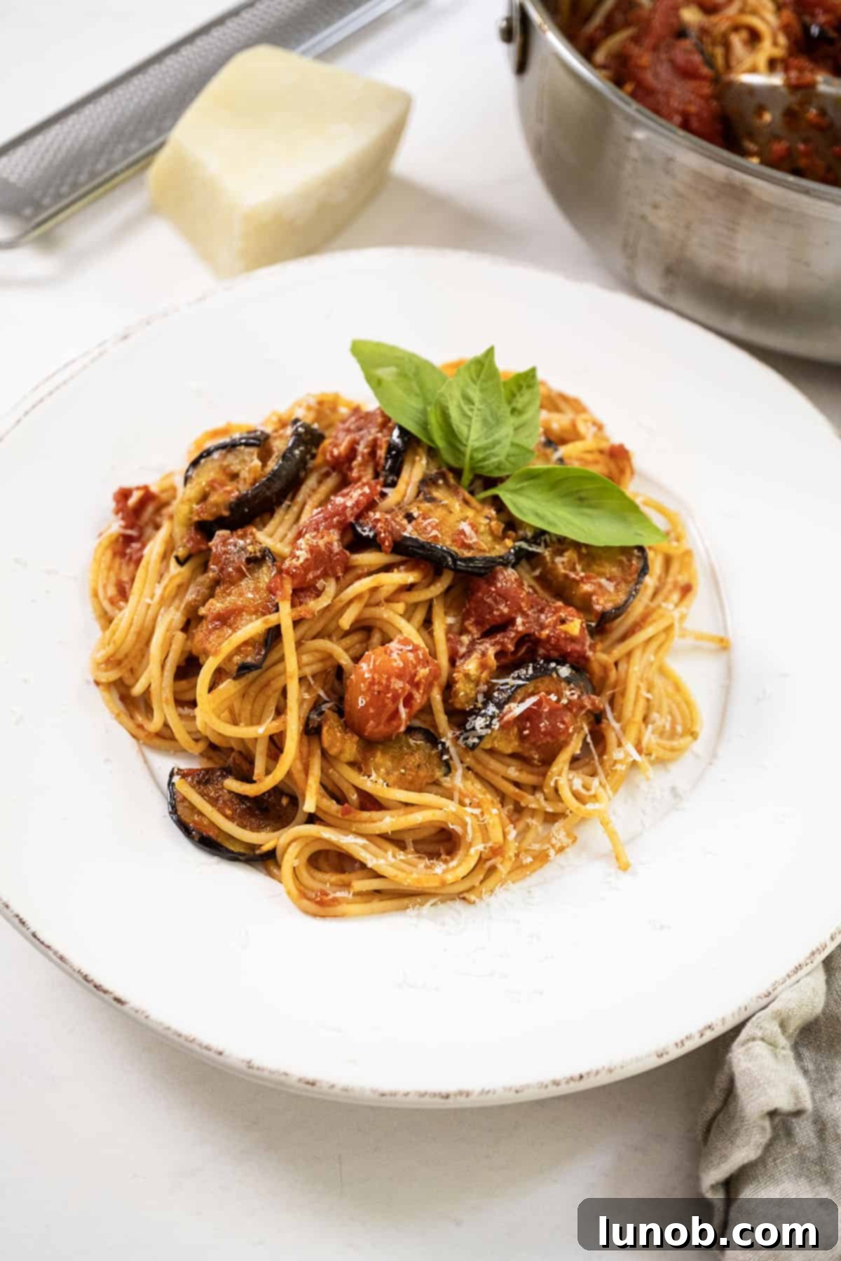 A close-up of Pasta alla Norma served on a white plate, adorned with fresh basil and grated cheese, ready to be enjoyed.
