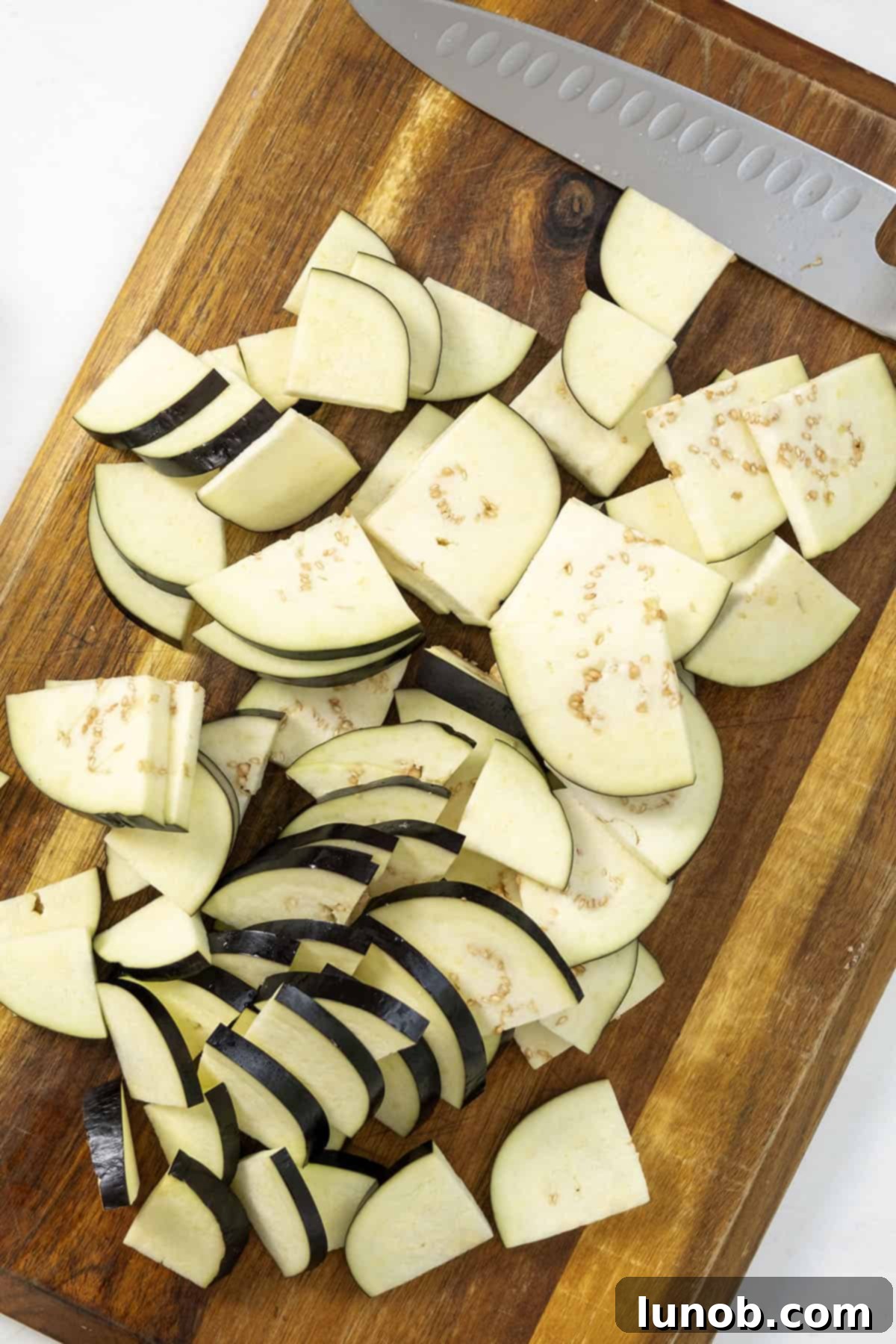 Eggplant slices, salted and then cut into quarters, resting on a wooden cutting board.