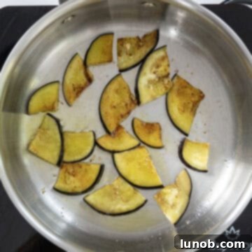 Small pieces of eggplant being fried to a golden brown in a large saucepan with olive oil.